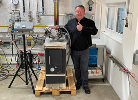 Mann mit Daumen hoch neben einem Mikro-BHKW aus Küchenherd