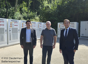 3 Personen vor Großbatteriespeicher